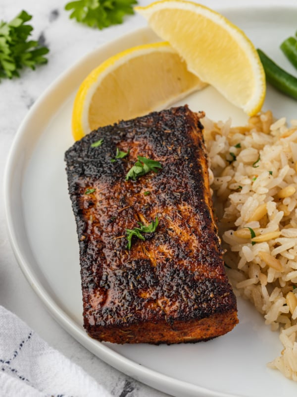 A blackened mahi mahi filet is plated with lemon slices and rice.