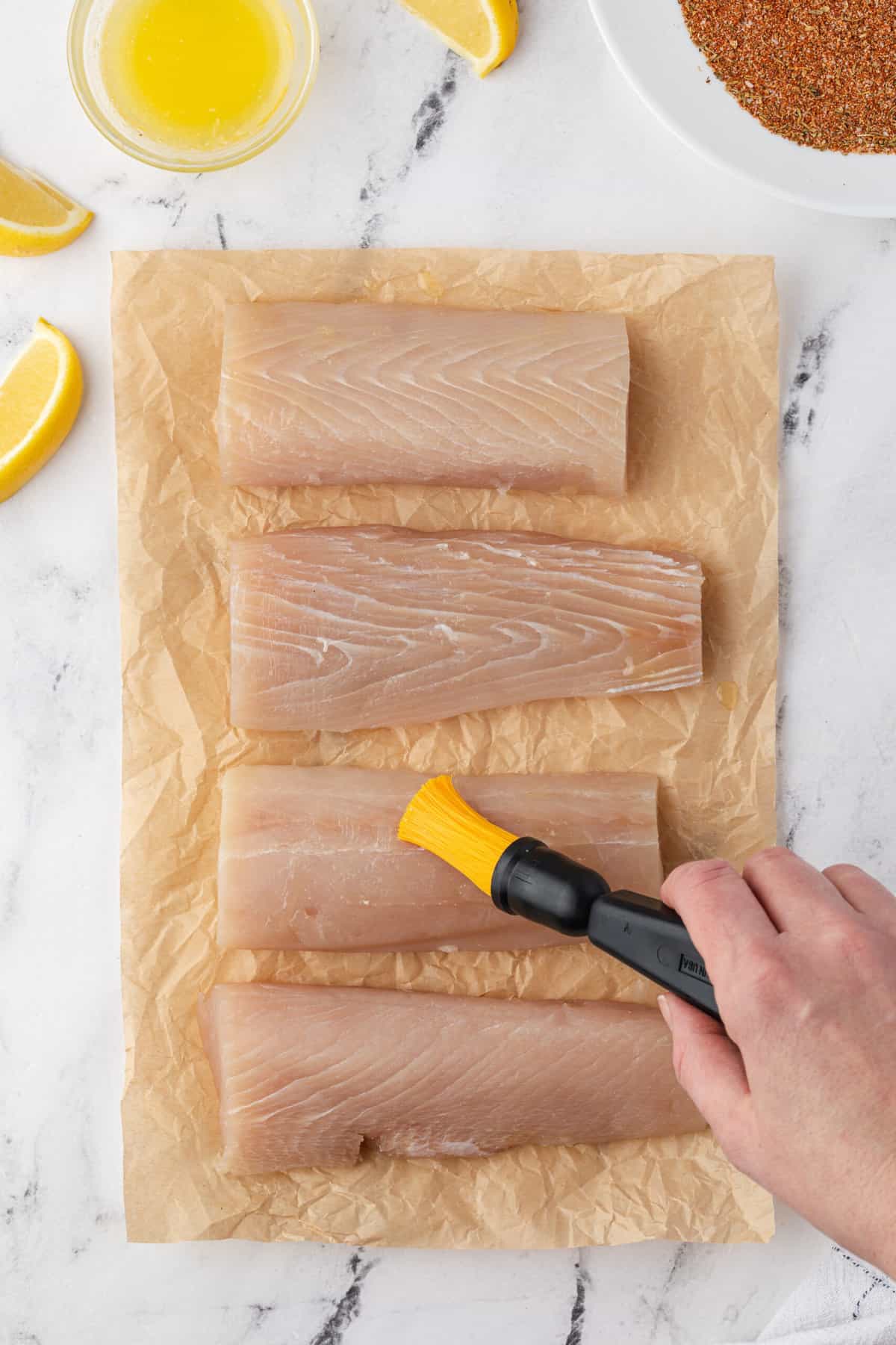 A brush is being used to coat butter on mahi mahi filets.