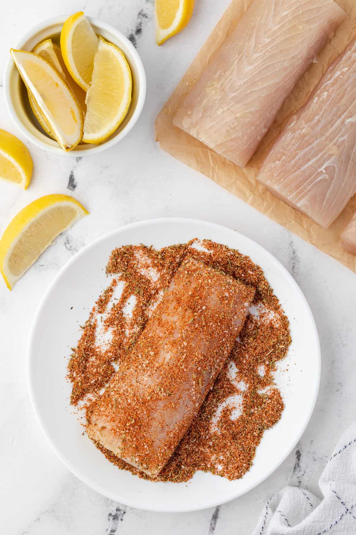 A piece of fish is being coated in seasoning on a white plate.