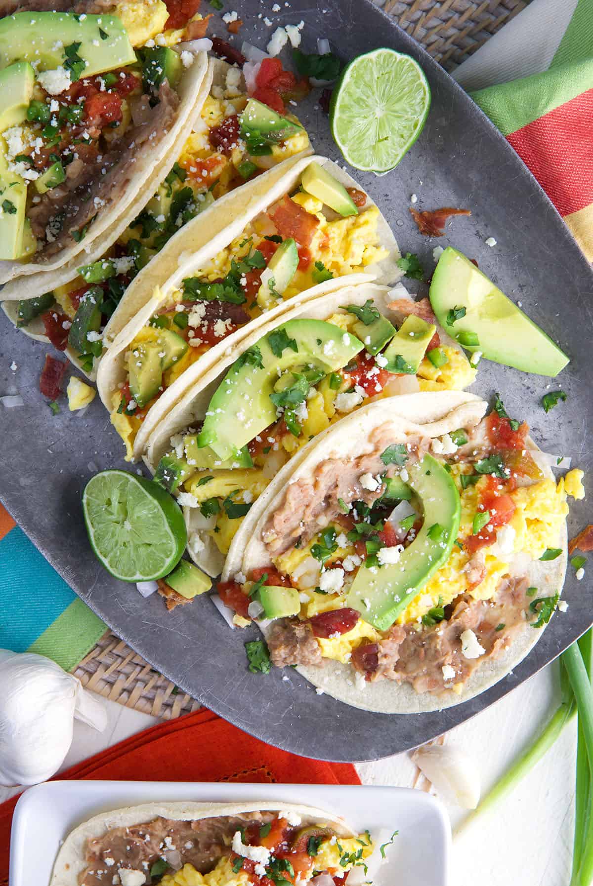 A plate full of breakfast tacos is presented next to some cut up limes.