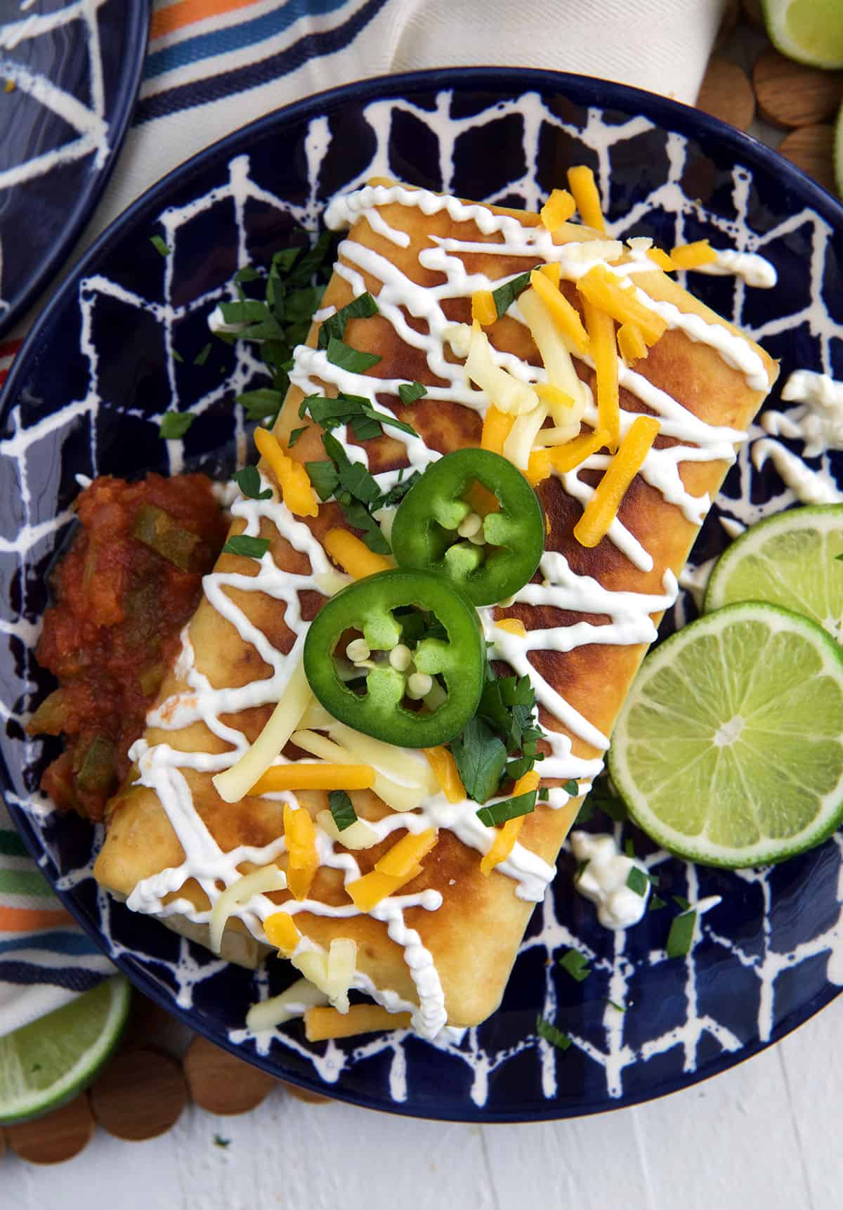 A fully garnished chimichanga is placed on a blue and white plate.