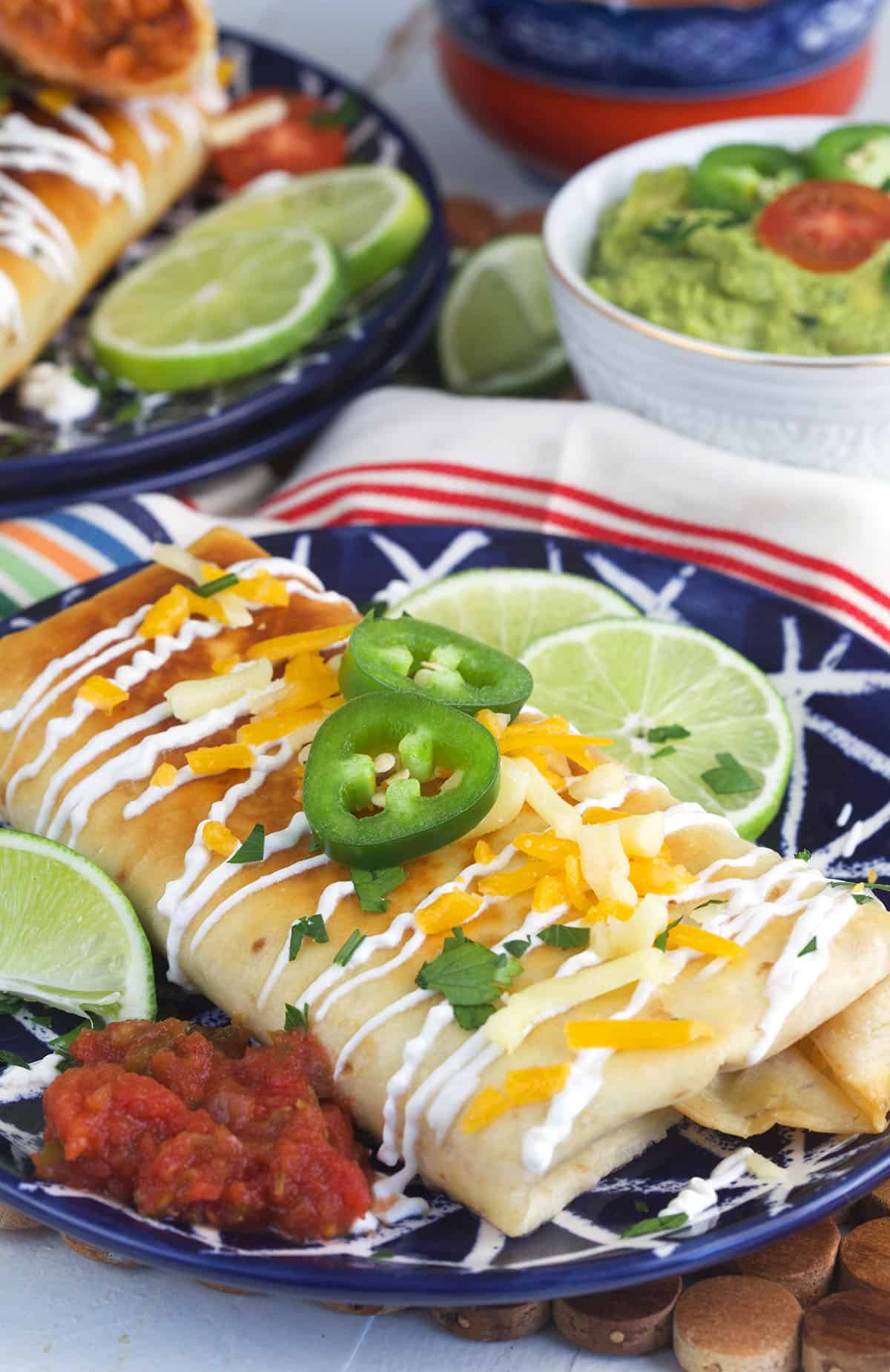 Garnished and plated chimichangas are plated next to salsa and limes.
