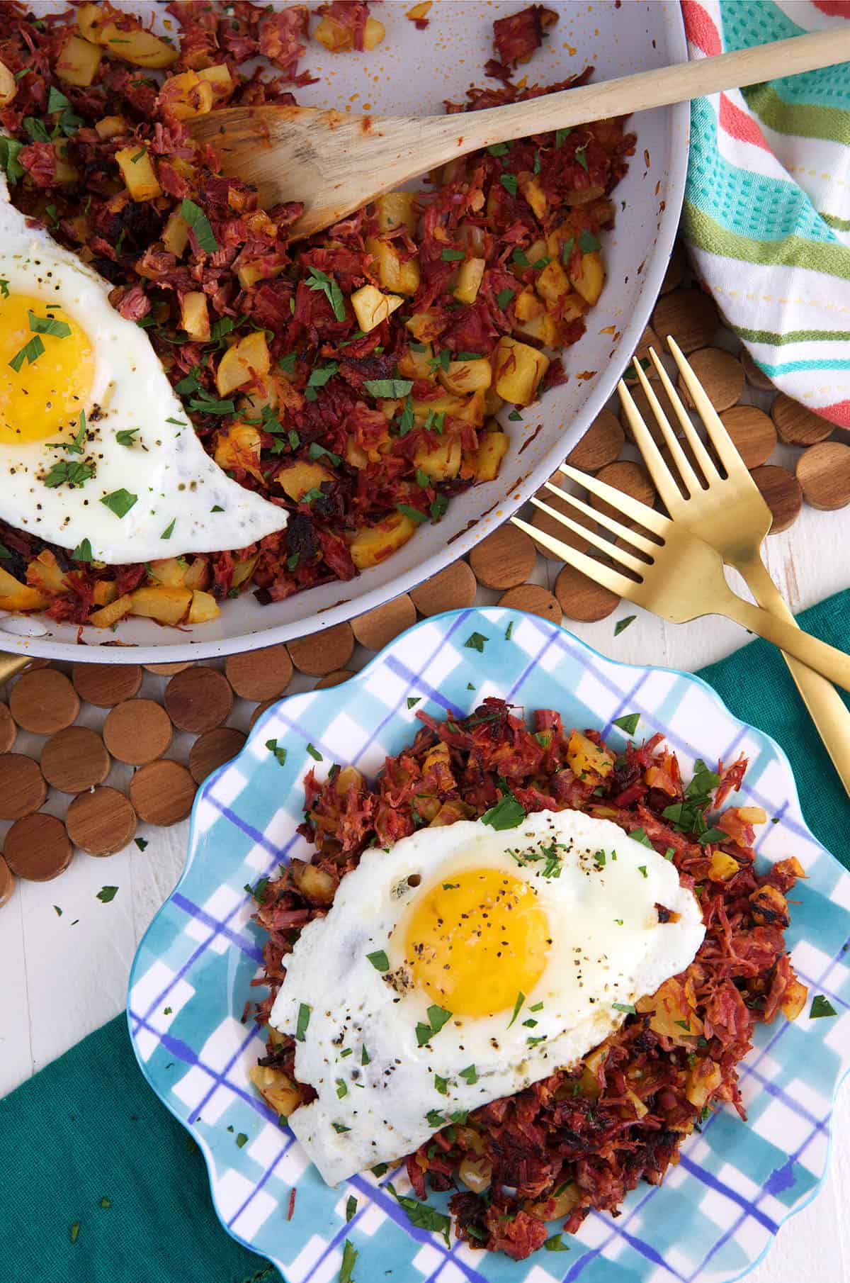 An egg is placed on top of a serving of hash next to a skillet filled with more hash.