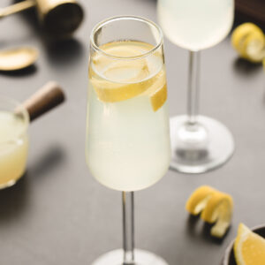 A glass of french 75 is garnished with a lemon peel.
