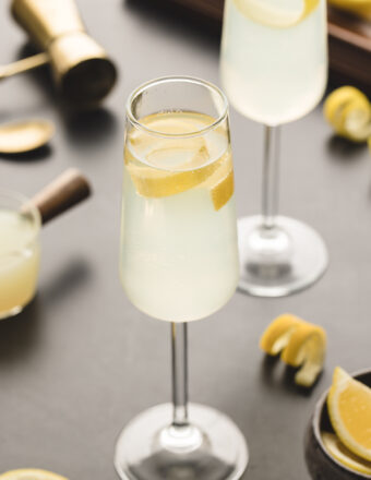 A glass of french 75 is garnished with a lemon peel.