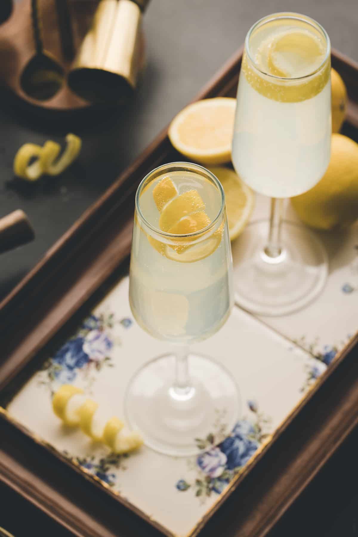 Two glasses of french 75 are placed on floral coasters. 