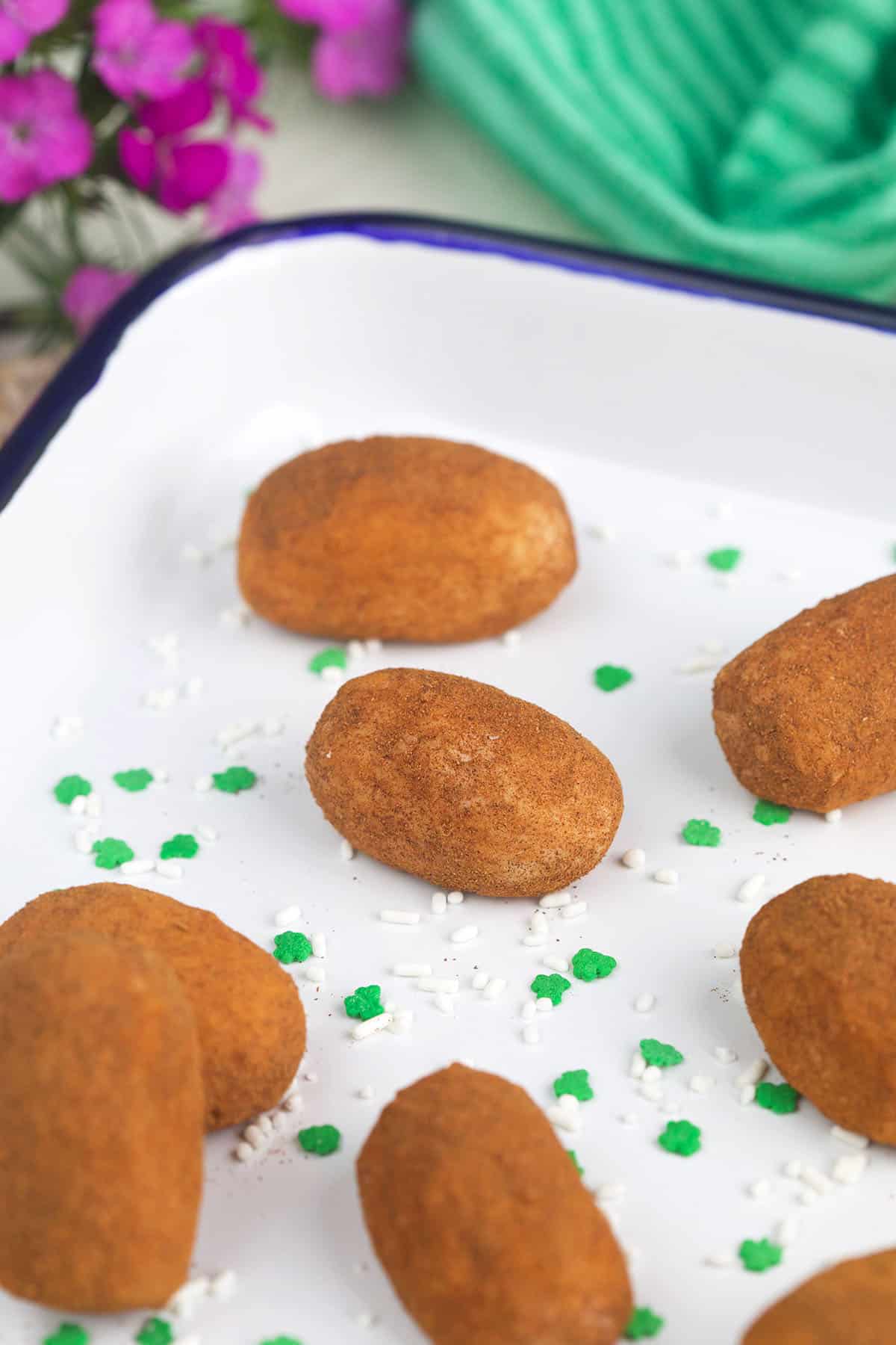 Several potato candies are placed in a white baking dish with shamrock sprinkles. 
