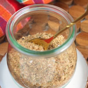A small spoon is placed in a glass jar filled with seasoning mix.