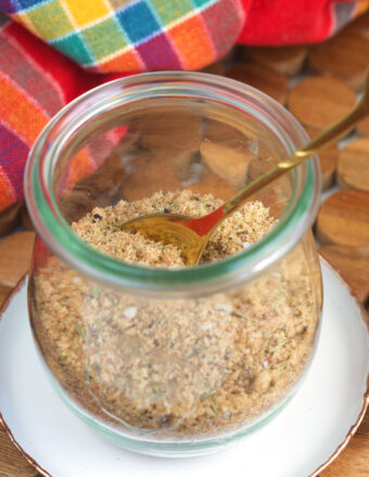 A small spoon is placed in a glass jar filled with seasoning mix.