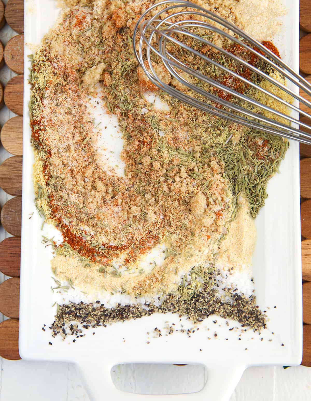A whisk is combining all of the seasoning blend ingredients on a white plate.