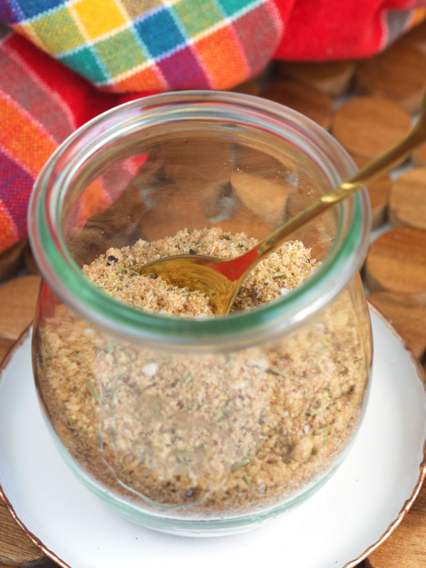 A small spoon is placed in a glass jar filled with seasoning mix.