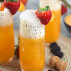 Several glasses are filled with peach bellini and garnished with strawberries.