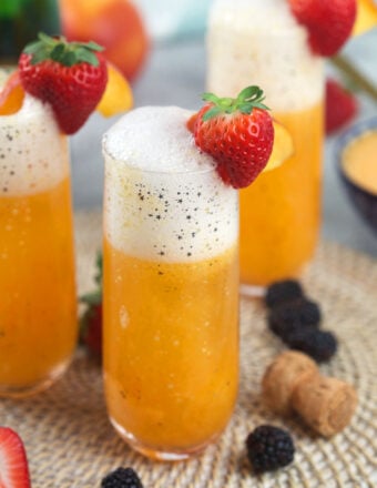 Several glasses are filled with peach bellini and garnished with strawberries.