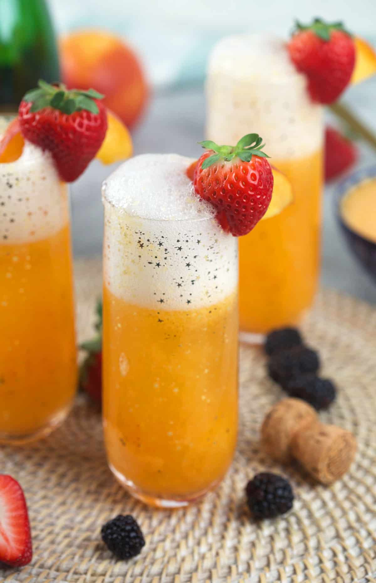 Several glasses are filled with peach bellini and garnished with strawberries. 