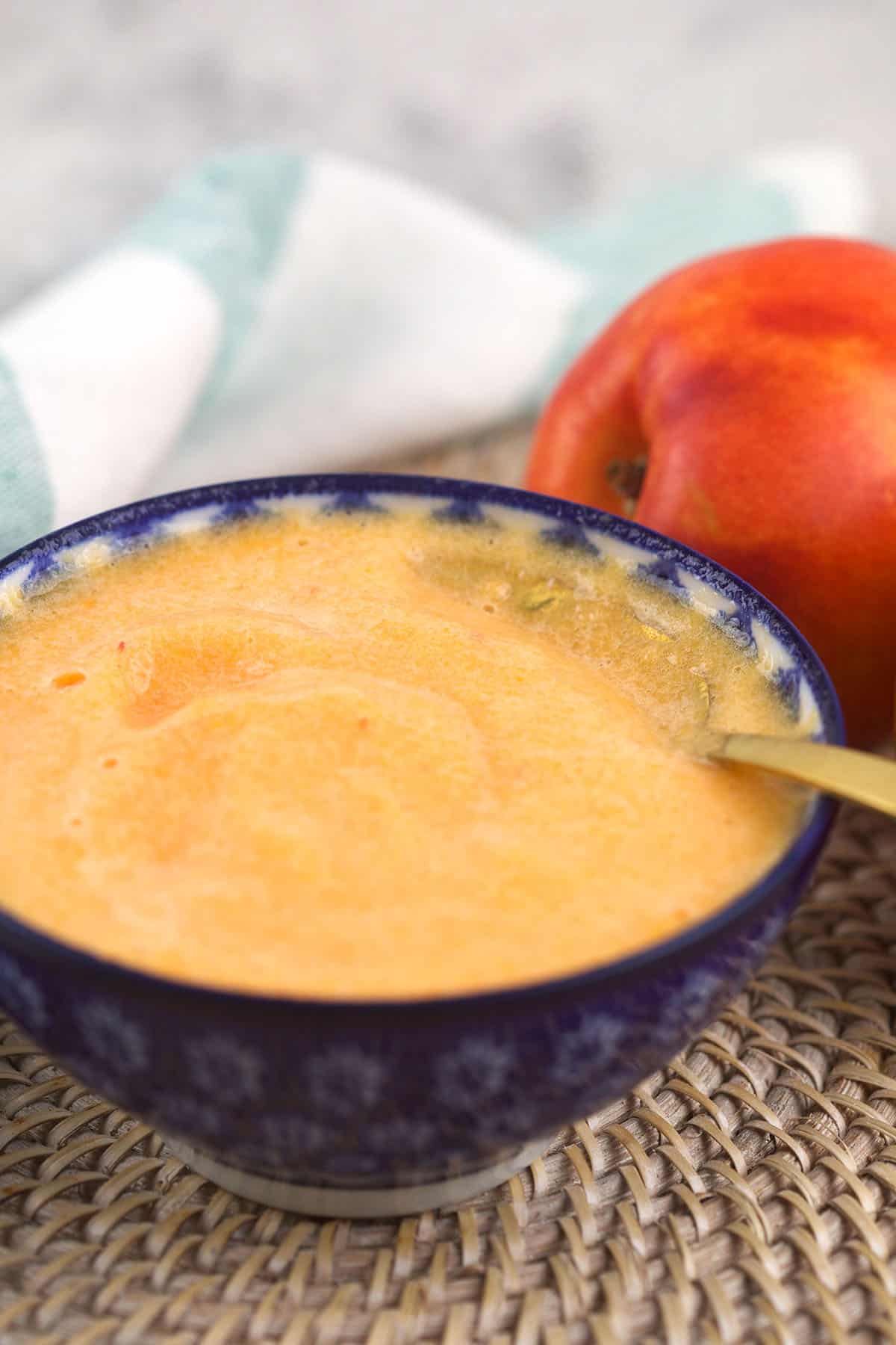 A bowl of peach puree is placed on a woven placemat. 