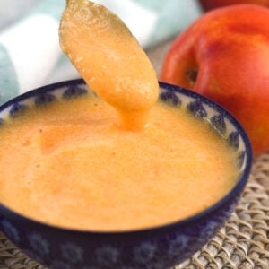 A spoon is being lifted from a small bowl filled with peach puree.