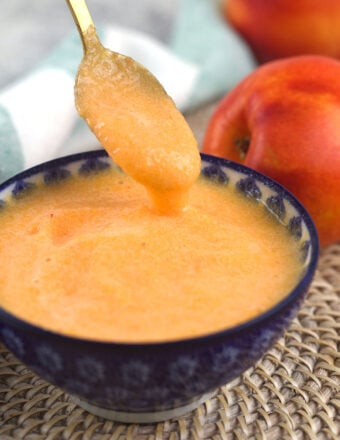 A spoon is being lifted from a small bowl filled with peach puree.