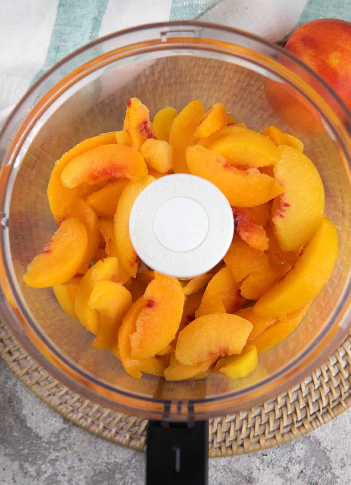Peaches are placed in the bowl of a food processor.