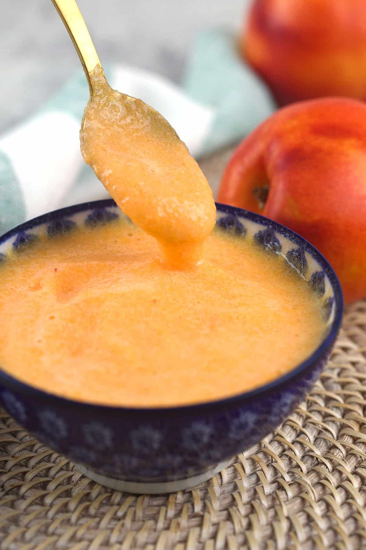 A spoon is being lifted from a small bowl filled with peach puree.
