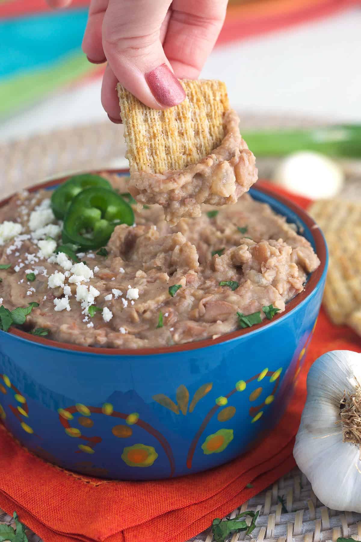 A cracker is being dipped into a bowl filled with refried beans.