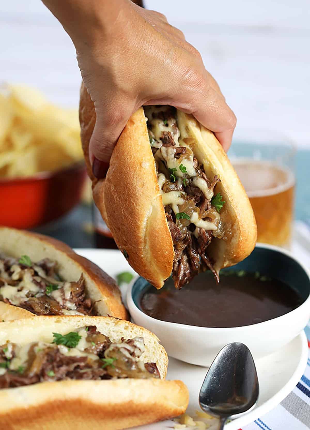 French dip Sandwich being dipped into a bowl of au jus sauce.