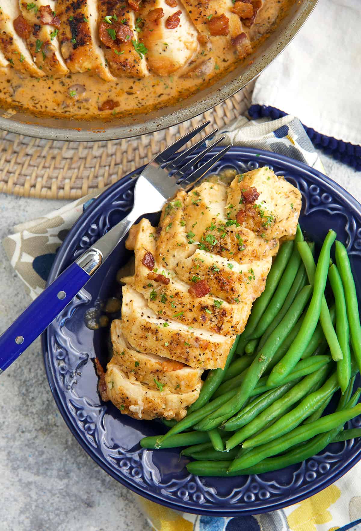 A sliced chicken breast is placed next to a serving of green beans. 