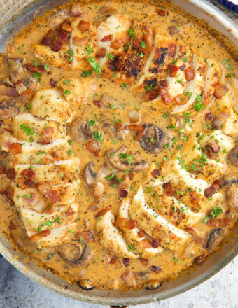 Several sliced chicken breasts are covered with gravy and placed in a skillet.