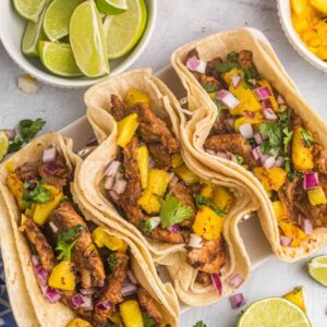 Three tacos are placed next to a few different garnishes.