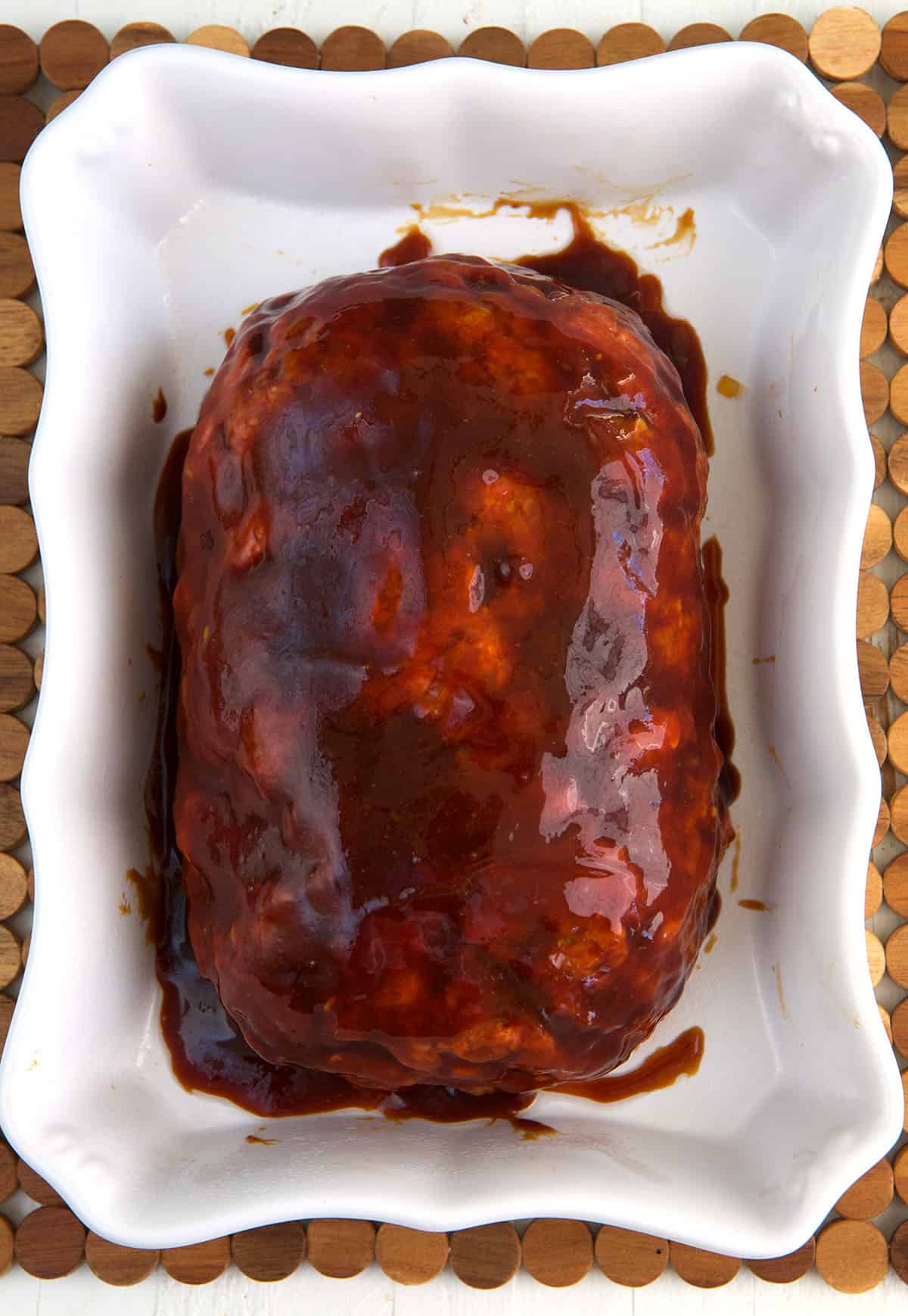 A prepared but unbaked meatloaf is placed on a baking dish.