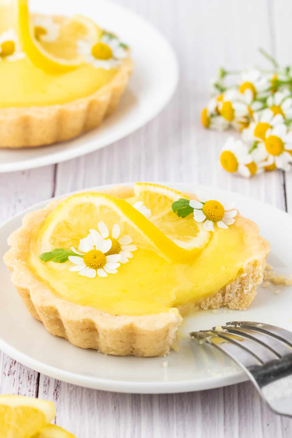 A fork is placed on a white plate next to a mini lemon tart.