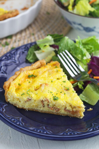 A piece of quiche is plated with a fork and a side salad.