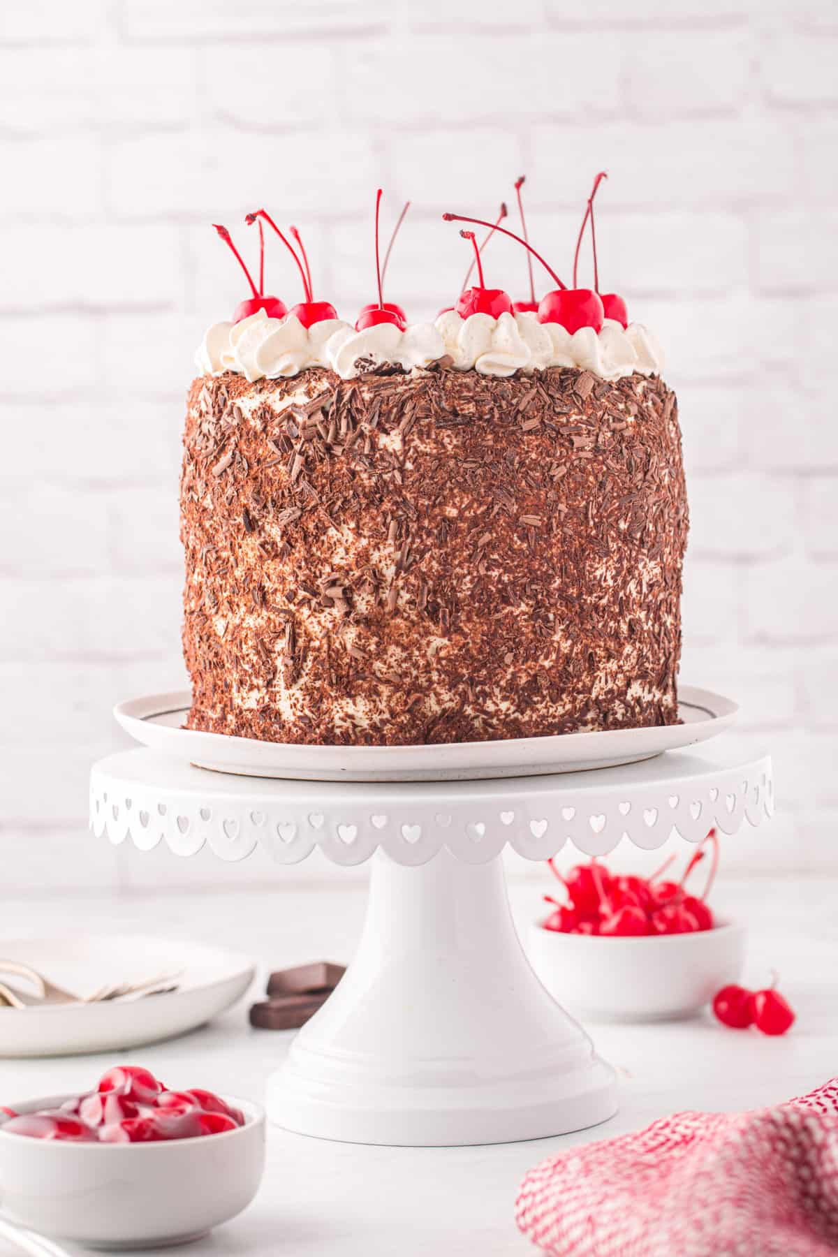 A white cake stand is holding a black forest cake.
