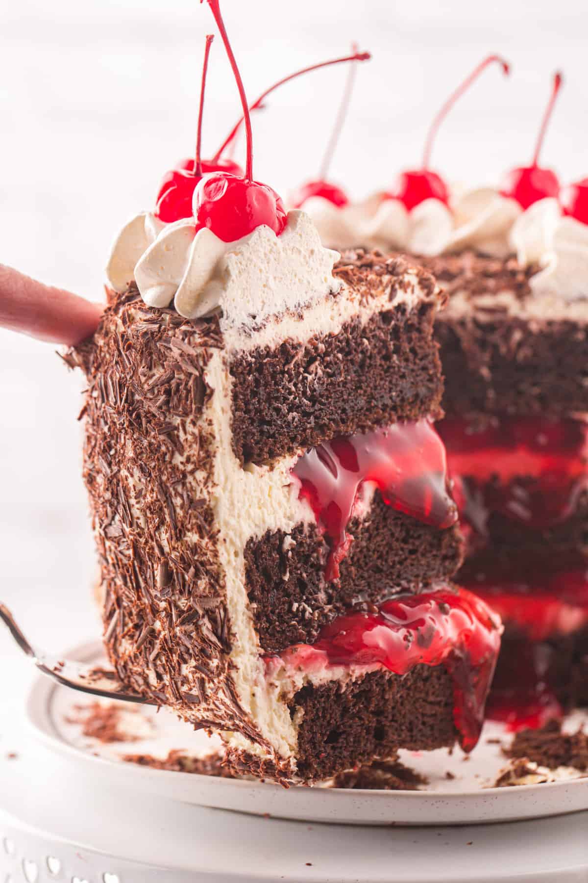 A slice of black forest cake is being removed from the cake stand.