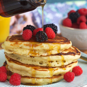 A stack of pancakes is being topped with maple syrup.