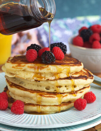 A stack of pancakes is being topped with maple syrup.