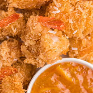 A batch of coconut shrimp are presented around a small bowl of dipping sauce.