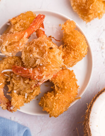 A round white plate is topped with several cooked coconut shrimp.