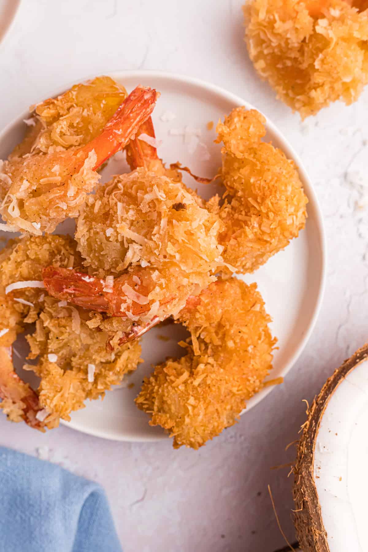 A round white plate is topped with several cooked coconut shrimp.