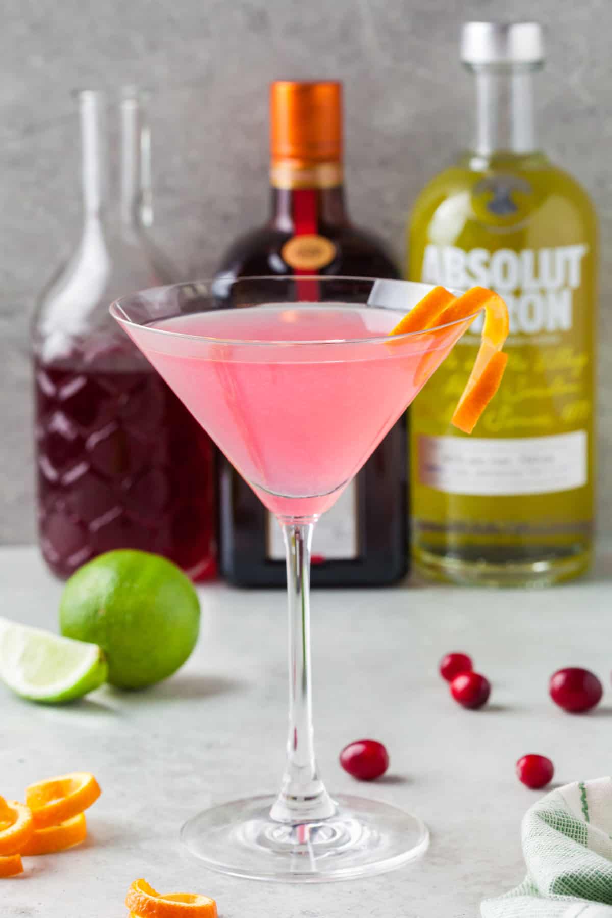 A garnished cosmopolitan is placed in front of other ingredients. 