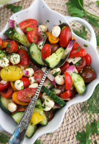 A white dish is filled with cucumber tomato salad.