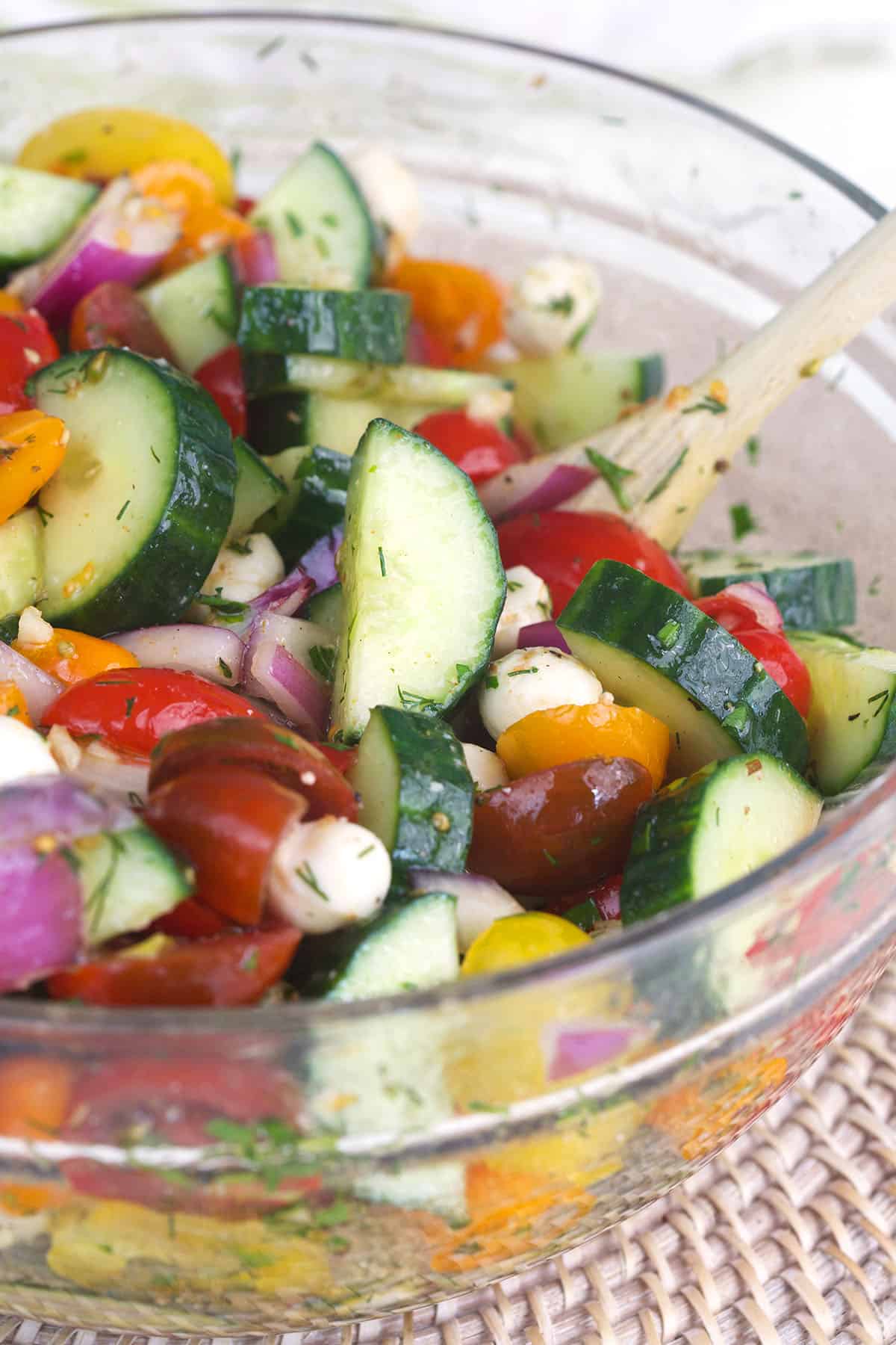 A cucumber tomato salad is being mixed in a large glass bowl. 