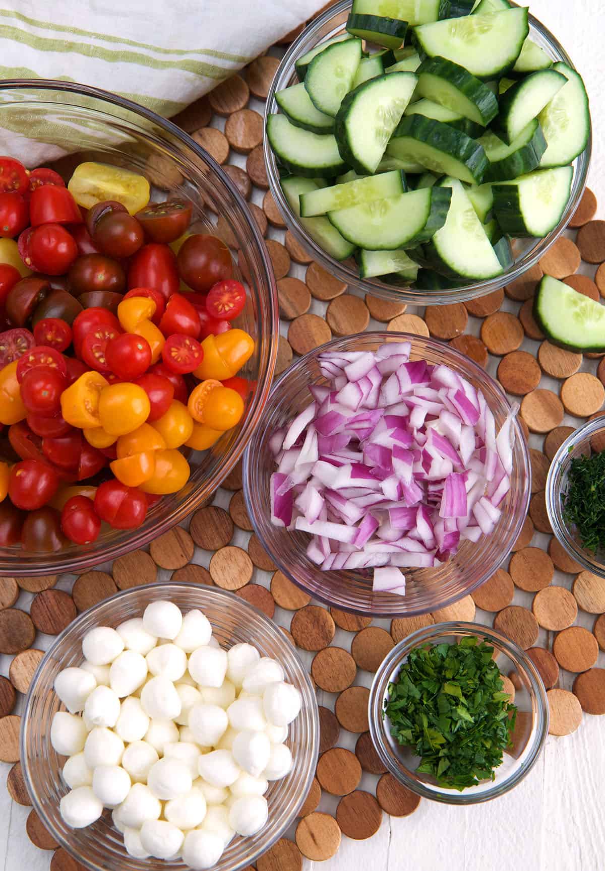 The ingredients for cucumber tomato salad are placed on a wooden place mat. 