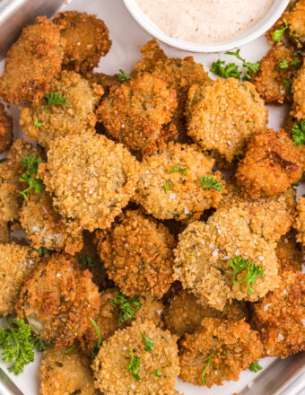 A batch of fried pickles is plated next to a cup of dipping sauce.