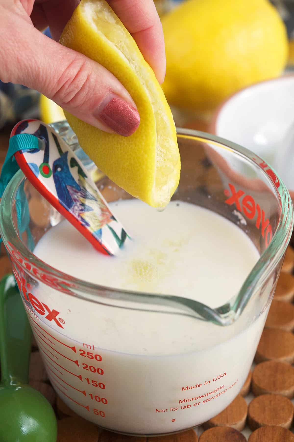 A lemon is being squeezed over a cup of milk.