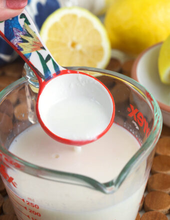 Vinegar is being poured into a glass measuring cup filled with milk.