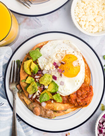 A serving of huevos rancheros is plated on a white and blue round plate.