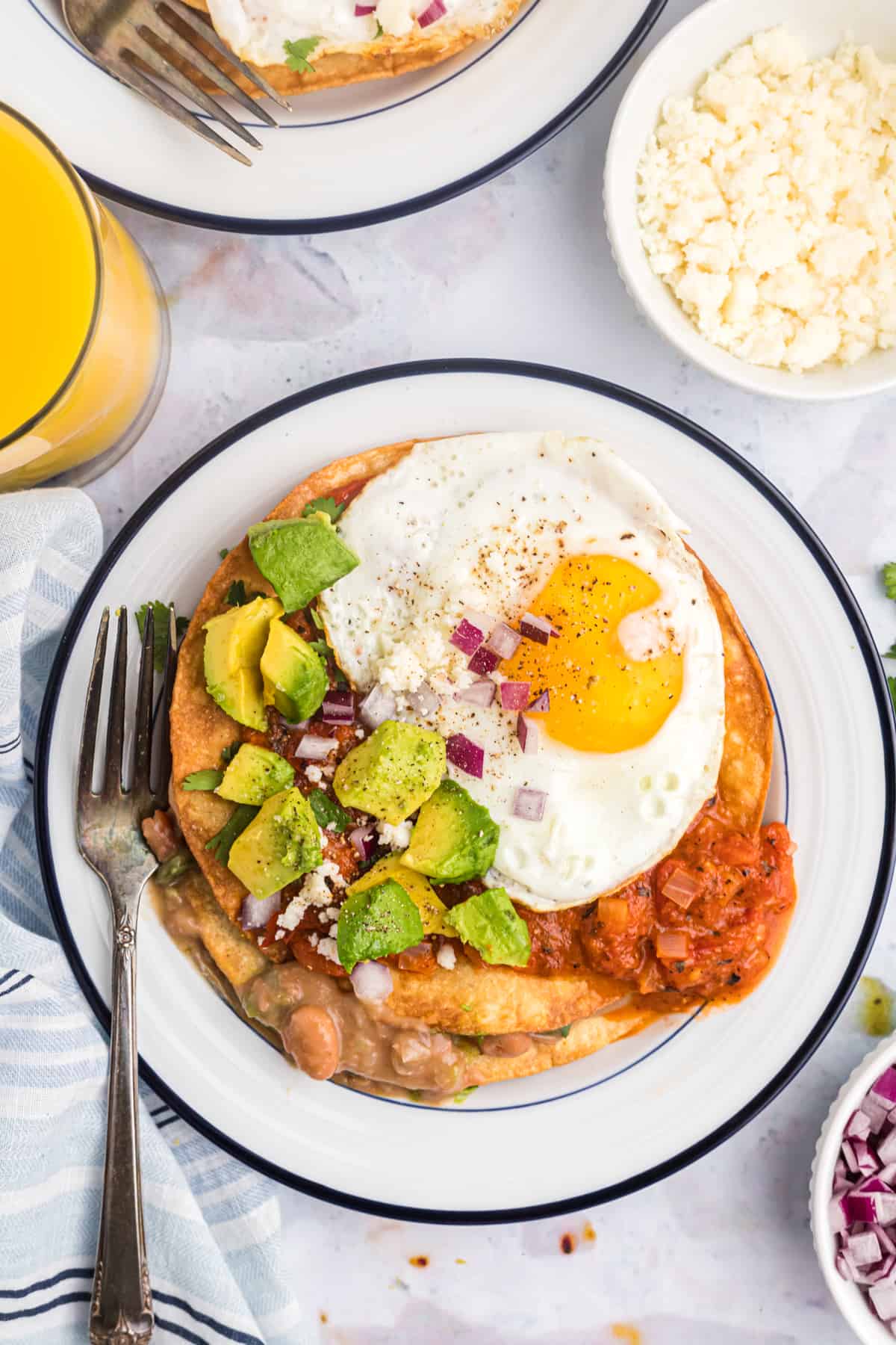 A serving of huevos rancheros is plated on a white and blue round plate.