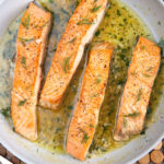 Four salmon filets are being cooked in a skillet.