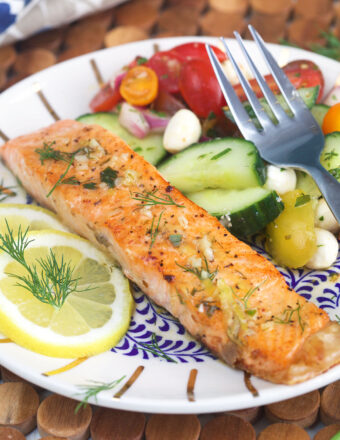 Salmon is plated next to a side of fresh vegetables.