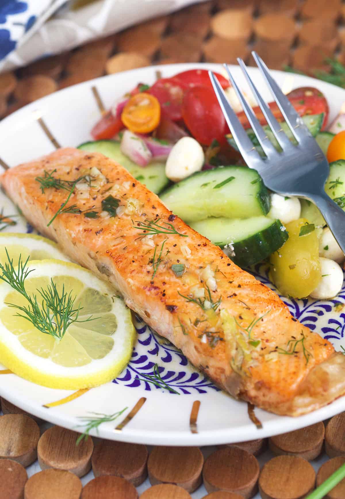 Salmon is plated next to a side of fresh vegetables. 